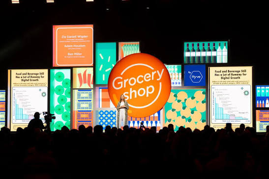 Woman giving a presentation on stage with Groceryshop logo in background