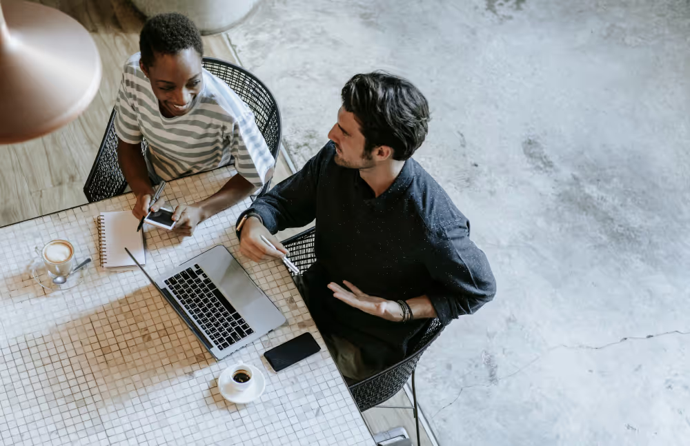 Man and woman sitting at a desk with a laptop and coffee cups.