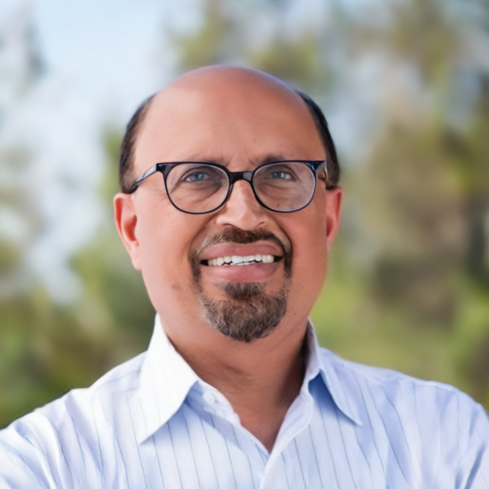 Ajay Chopra wearing glasses and a blue shirt with a white collar.
