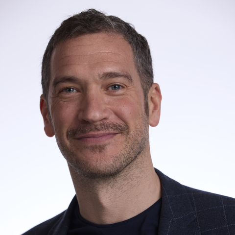 Daniel Shering smiling in a black shirt and blue jacket