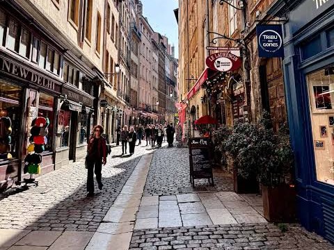 People walk down a cobblestone street with many shops on either side.