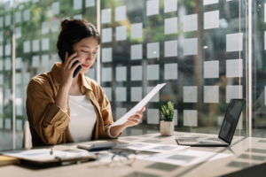 Woman in office holding paper and speaking on phone, reviewing documents.