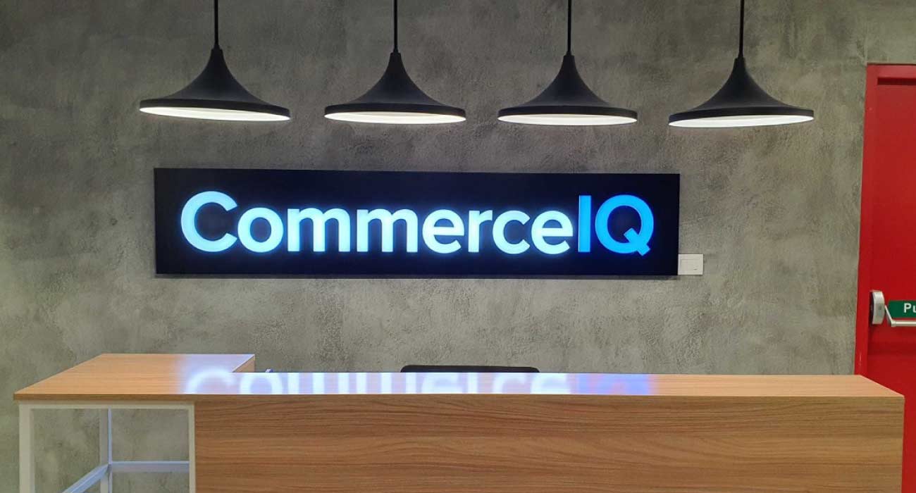 CommerceIQ logo illuminated on a modern office wall above a reception desk.
