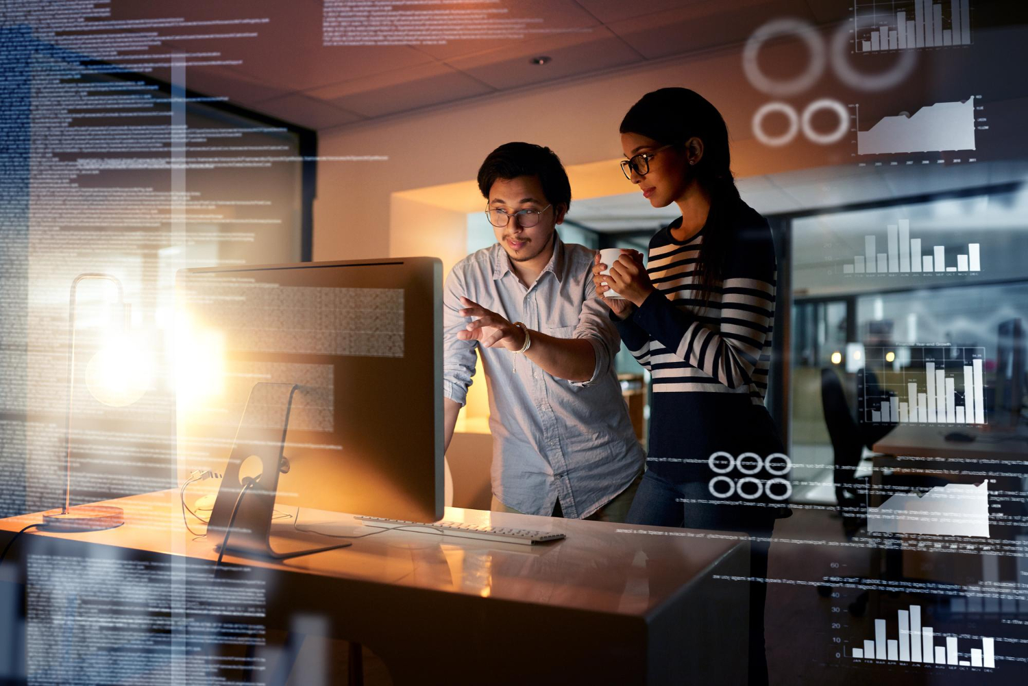 Two people analyzing data on a computer screen with graphs and charts in the background.